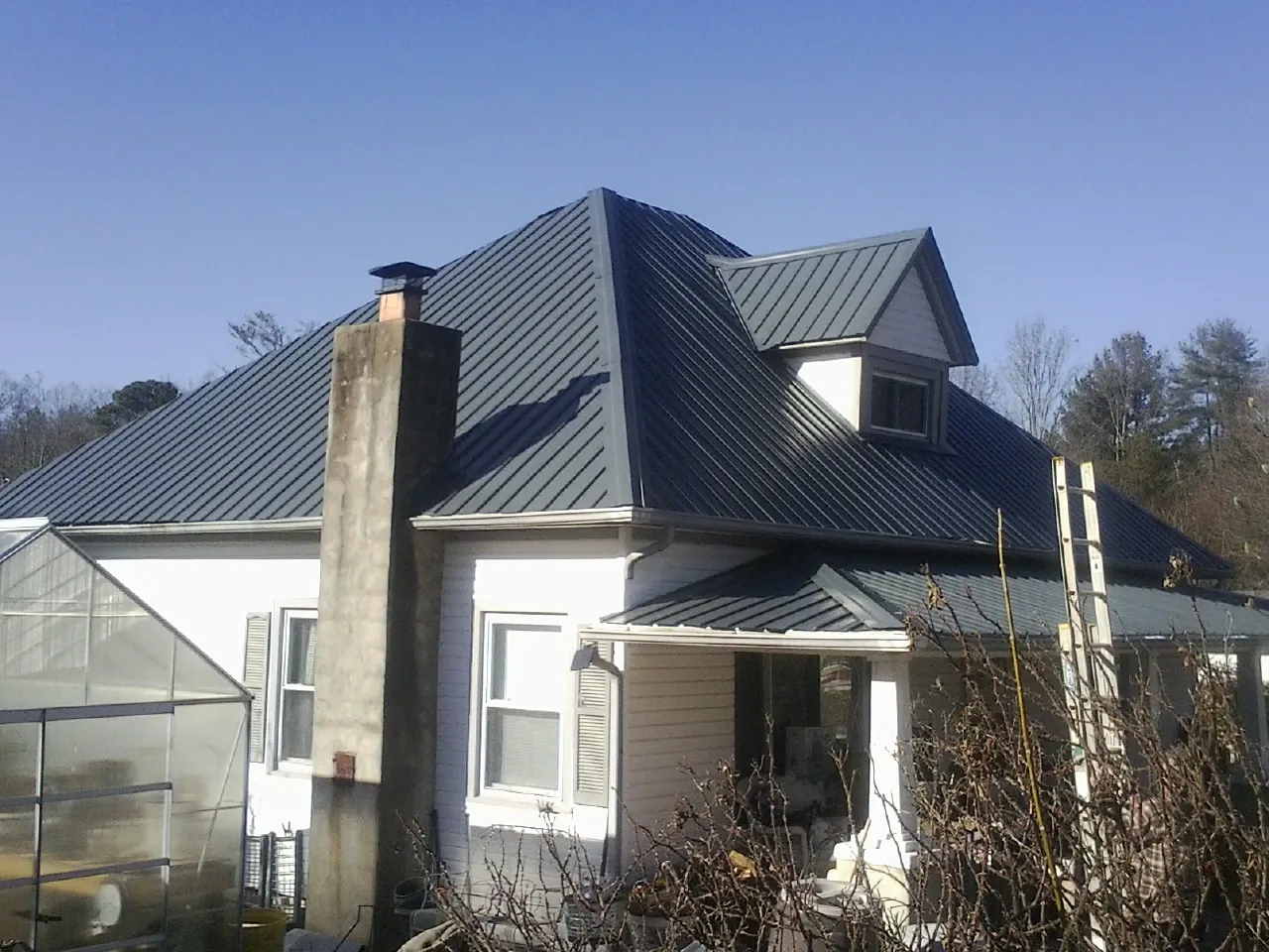 Dark blue standing seam metal roof on a white farmhouse with dormer — Slate & Tile Roof Repair by Roofing Brothers in Marshville