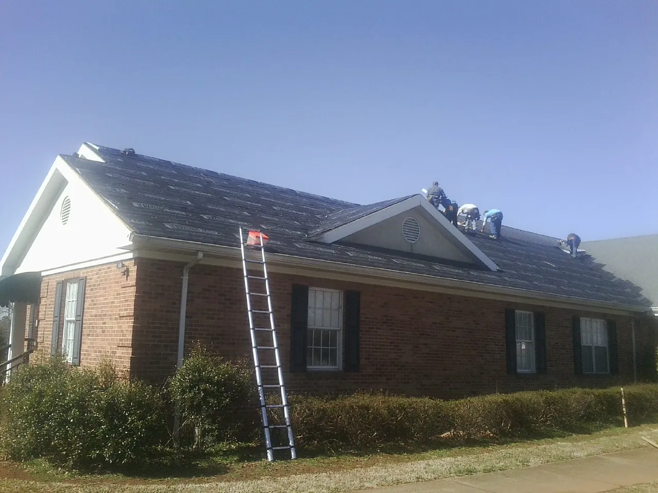 Crew tearing shingles off a brick ranch roof with a ladder set — Metal Roof Repair work by our crew in Marshville