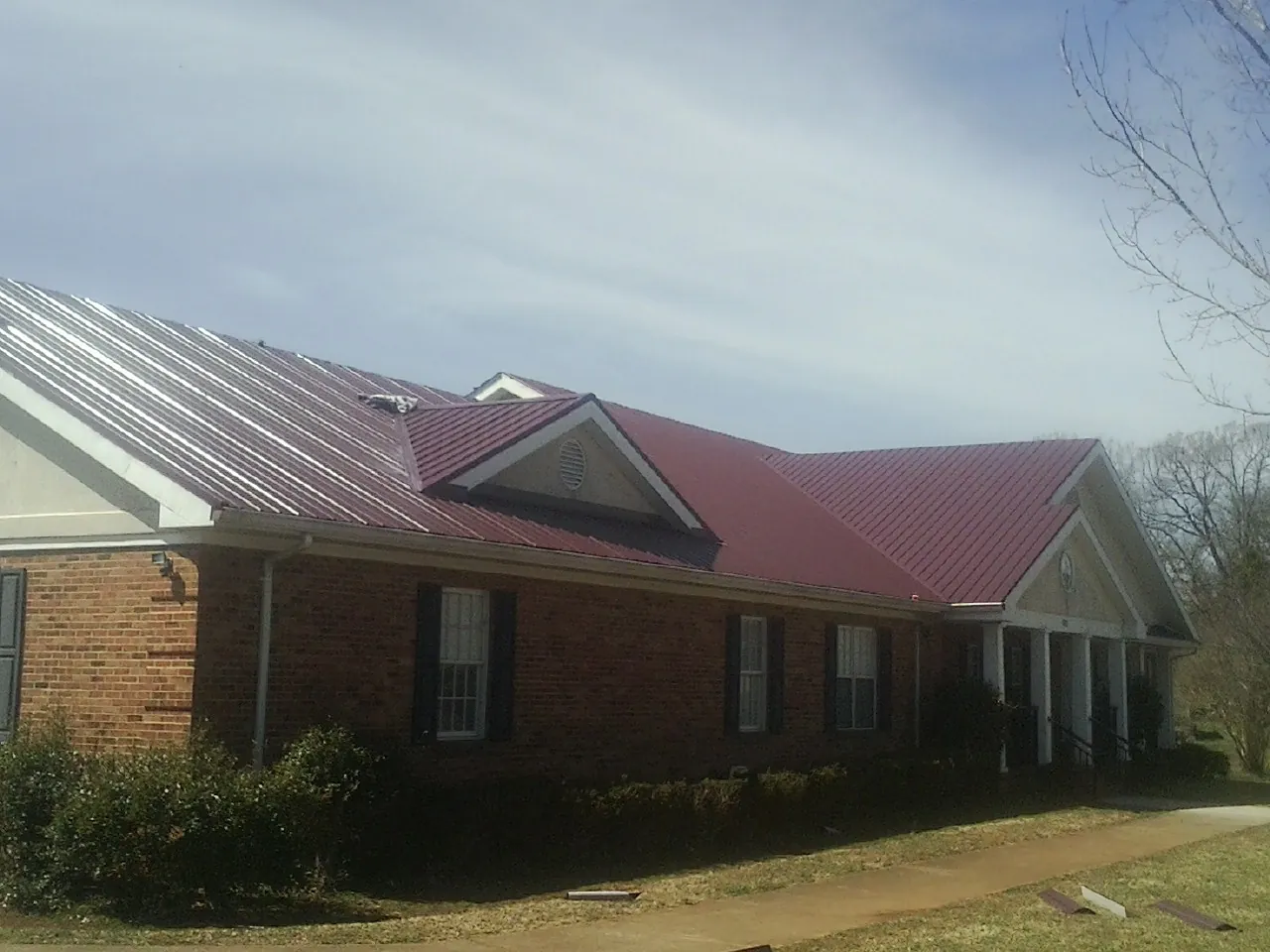 Red metal roof with gabled entries on a long brick building, from a Hail Damage Roof Repair job in Marshville