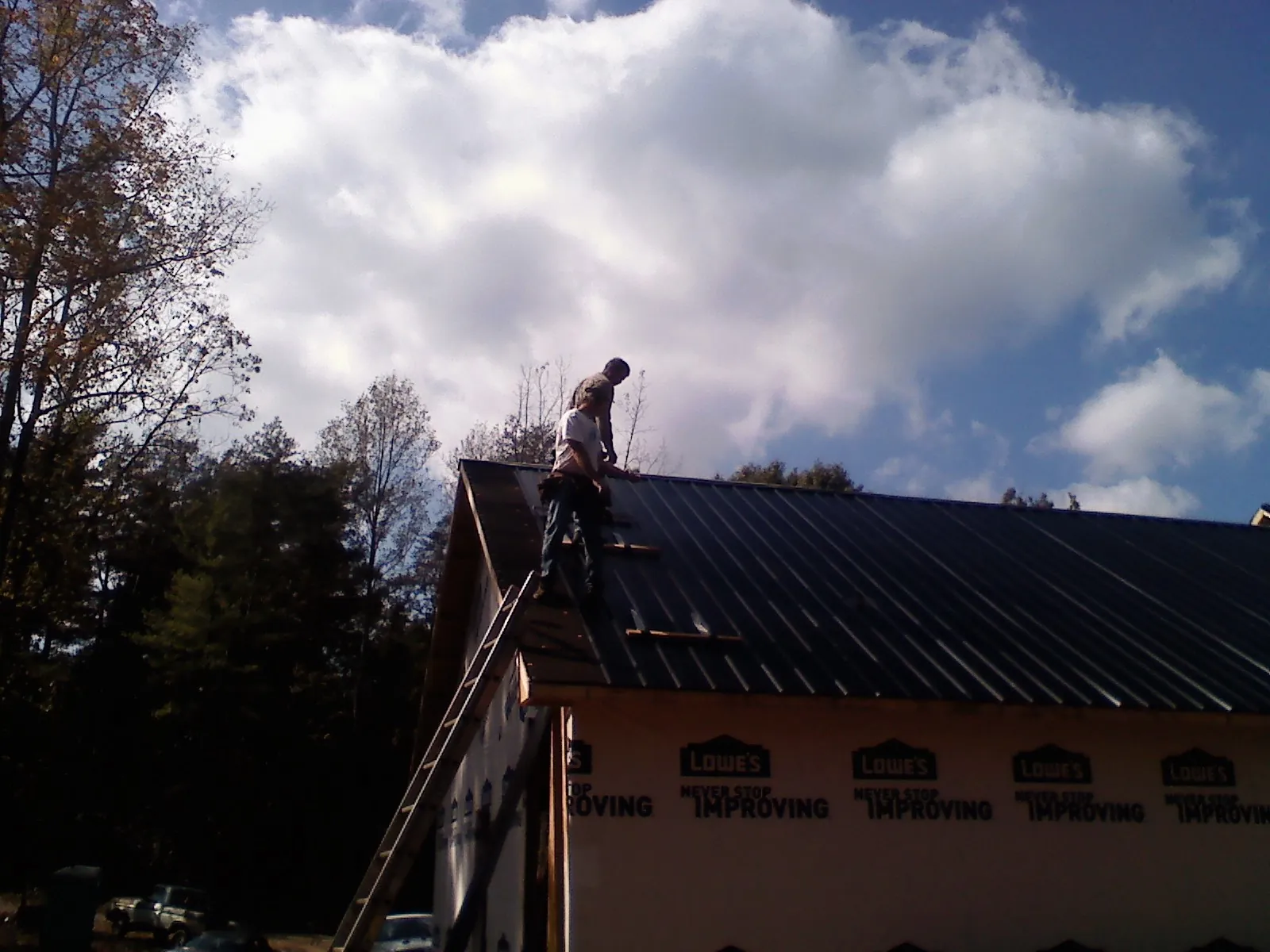Roofer fastening dark metal panels high against a cloudy sky, from a Roof Inspection job in Marshville