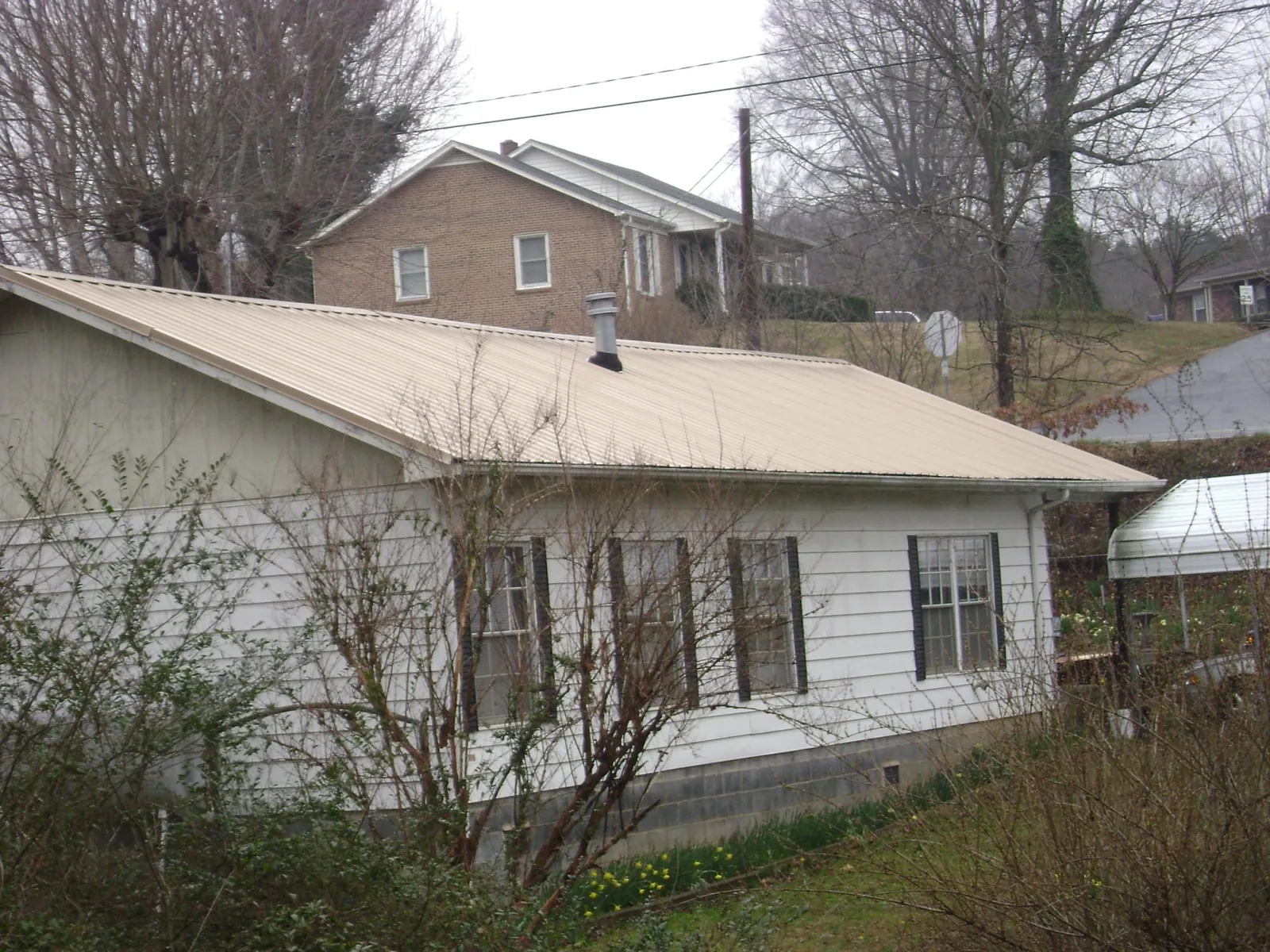 Tan metal roof on a white sided house set into a hillside — Commercial Roofing by Roofing Brothers in Marshville